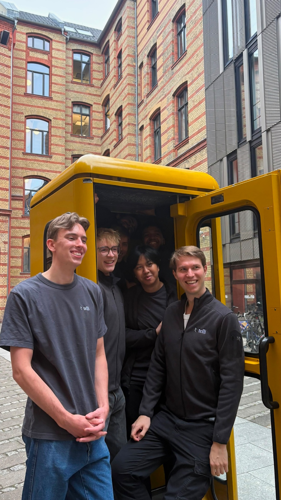 Team squeezed into a yellow Berlin phone booth
